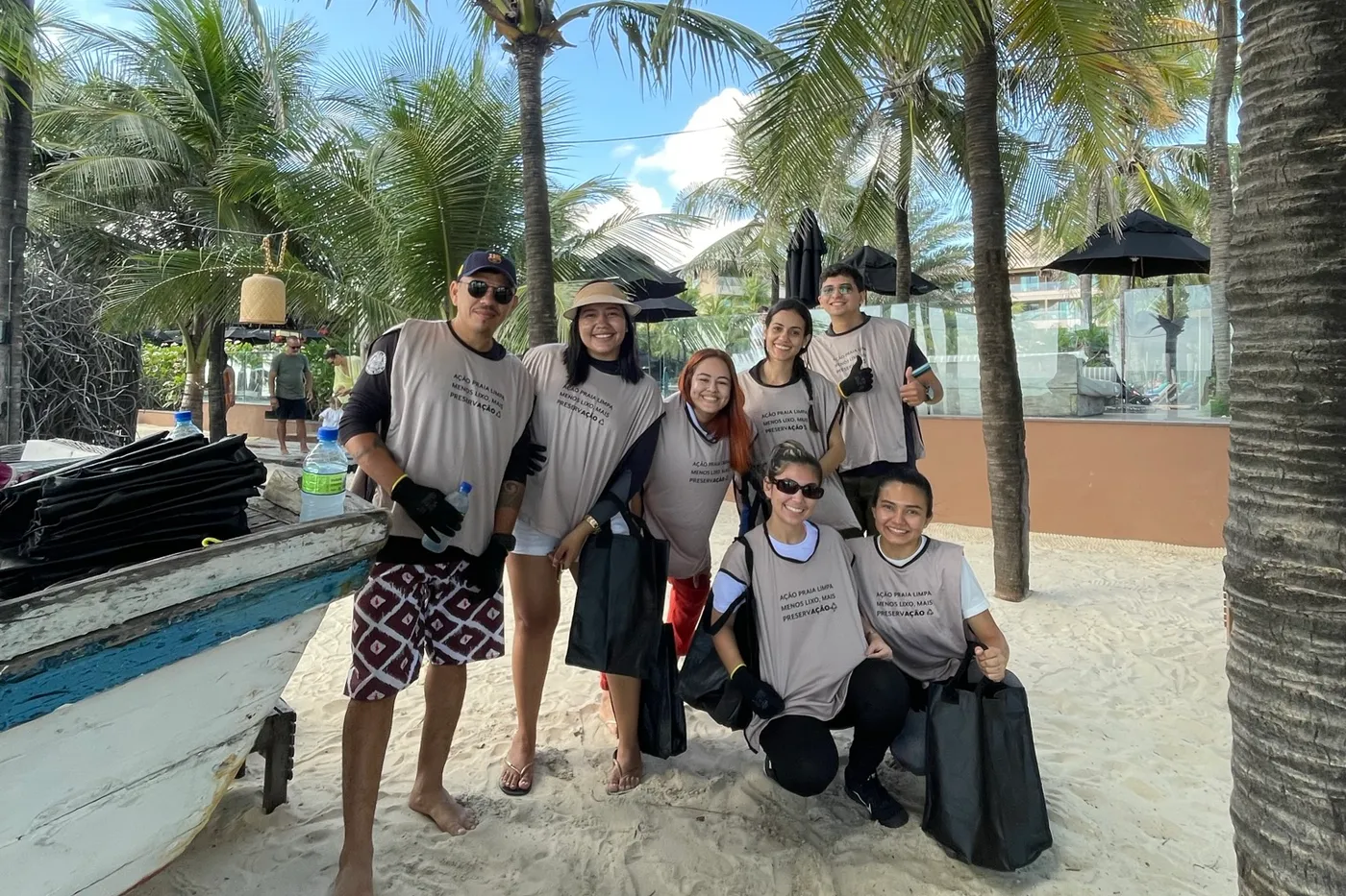 Colaboradores da Carmel Hotéis reunidos na praia, junto a um barco de pesca